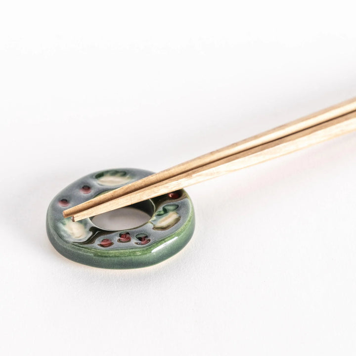 Green wreath shaped ceramic chopstick rest with detailed leaves adding festive touch to table.