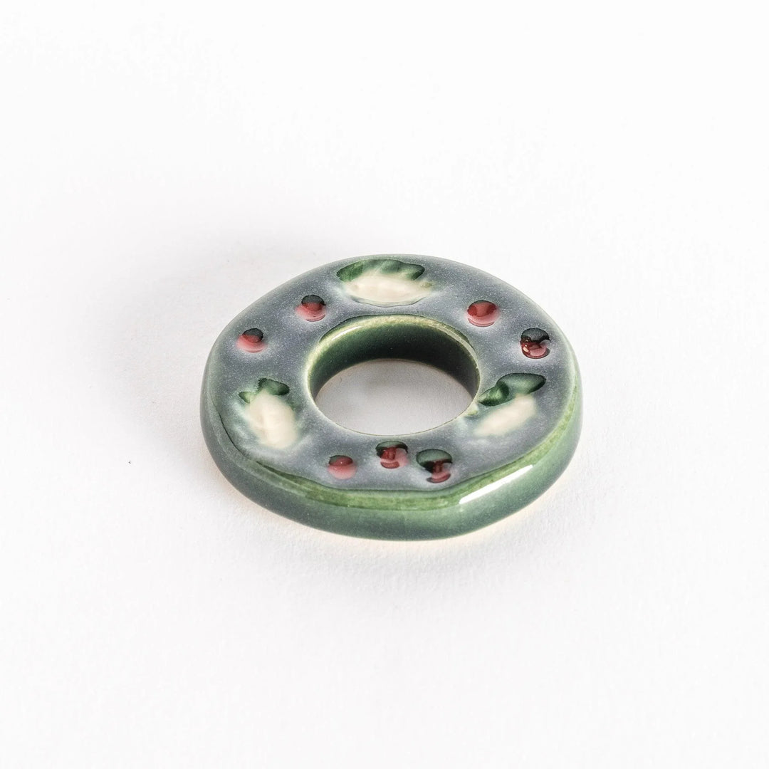 A slightly angled view of the ceramic green wreath chopstick rest, emphasizing its circular shape and glossy texture.