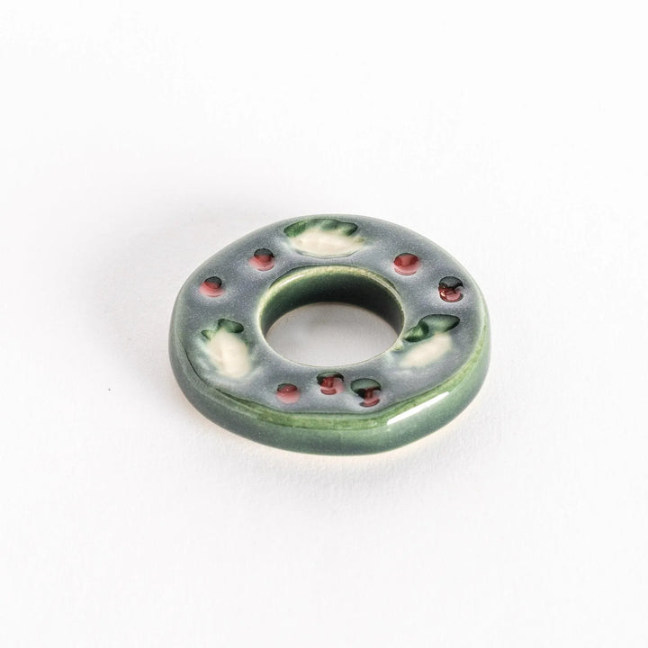 A slightly angled view of the ceramic green wreath chopstick rest, emphasizing its circular shape and glossy texture.