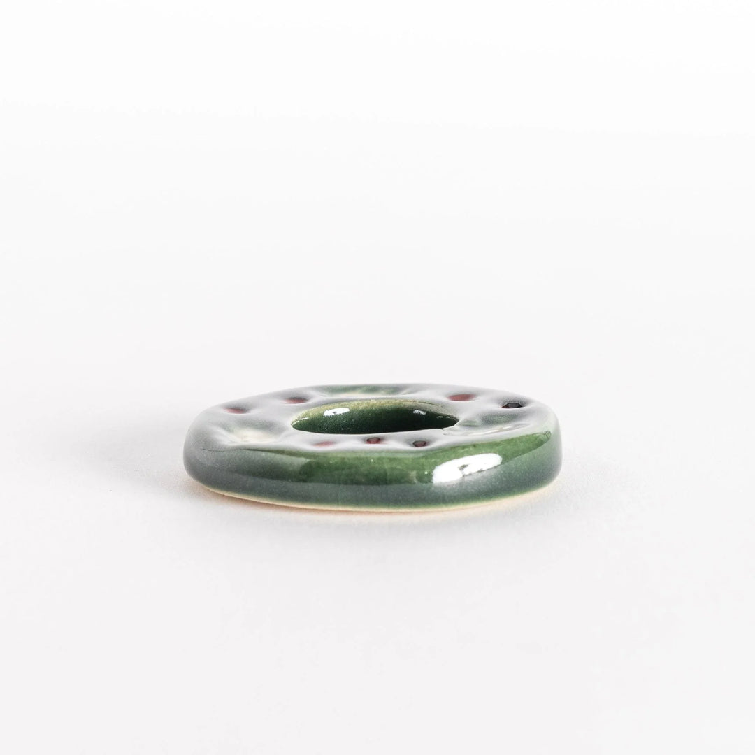 Green wreath shaped ceramic chopstick rest with detailed leaves adding festive touch to table.