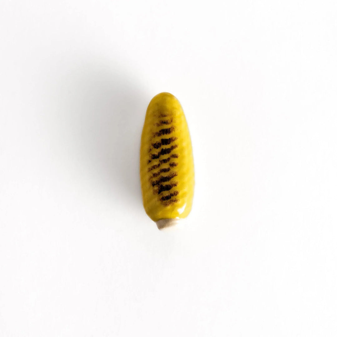 Grilled corn chopstick rest with charred yellow surface and lifelike details adding fun to table setting.
