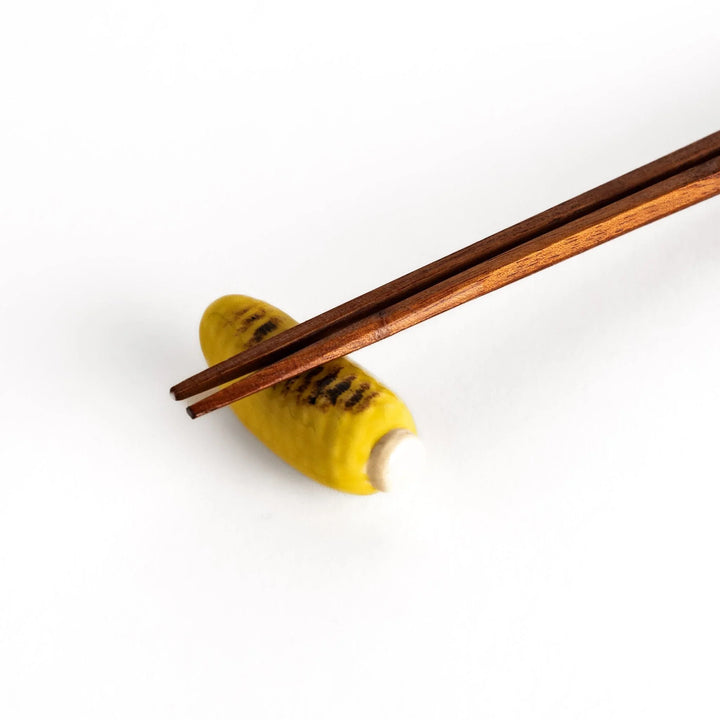 Grilled corn chopstick rest with charred yellow surface and lifelike details adding fun to table setting.