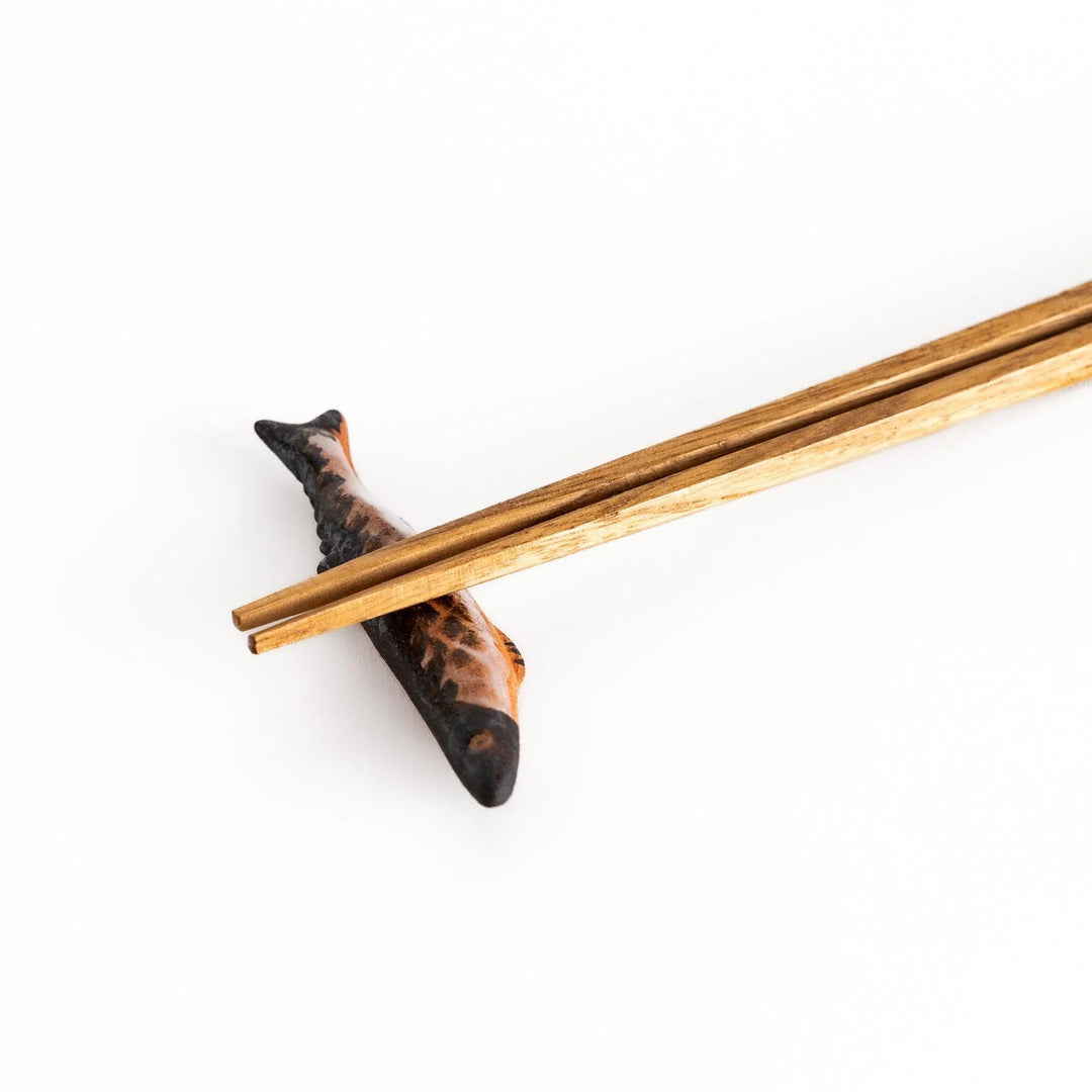 Ceramic chopstick rest shaped like grilled Pacific saury with textured glaze for realistic dining accent.
