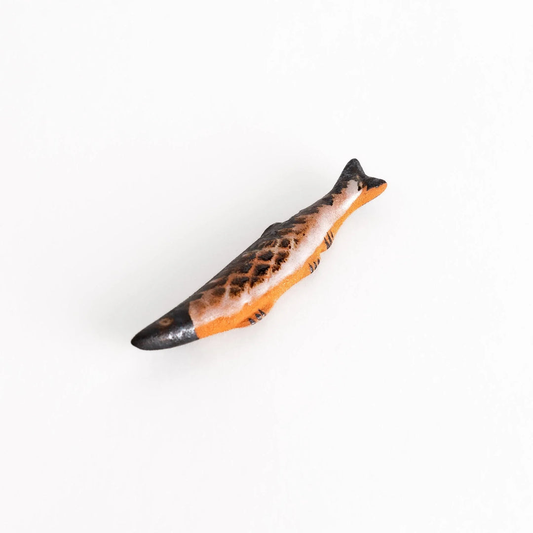 Ceramic chopstick rest shaped like grilled Pacific saury with textured glaze for realistic dining accent.