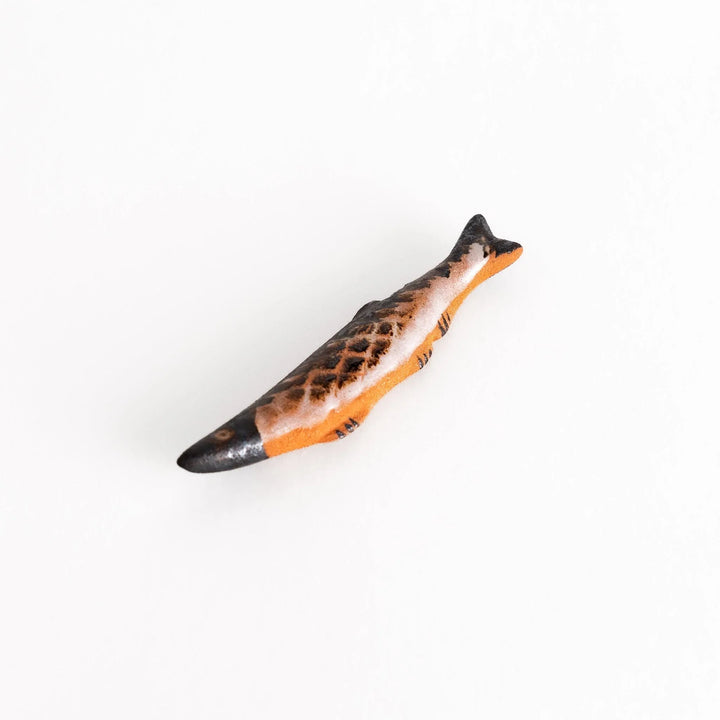 Ceramic chopstick rest shaped like grilled Pacific saury with textured glaze for realistic dining accent.