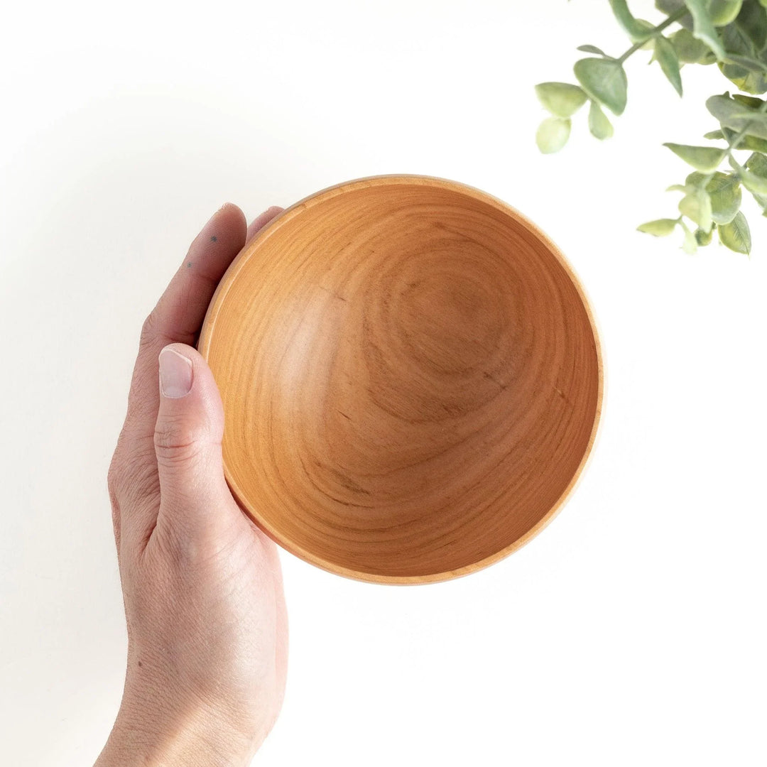 A hand holding a handcrafted wooden bowl, showcasing its warm color and natural grain, ideal for daily use.
