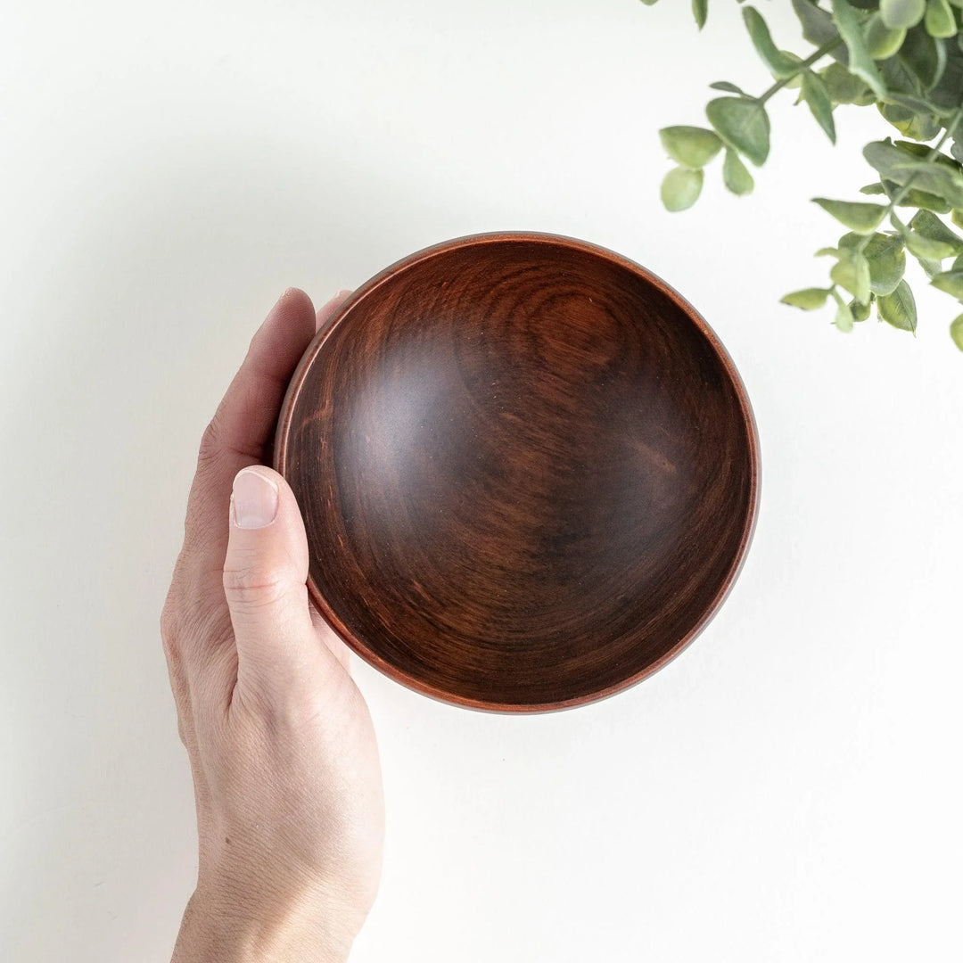 A hand holding the handcrafted brown wooden bowl, showcasing its sleek interior and natural wood finish.