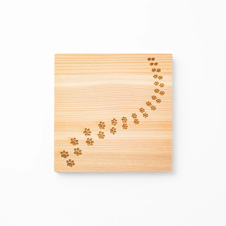 Square hinoki wood trivet featuring curved trail of laser-cut cat paw prints, protecting surfaces with charming feline design