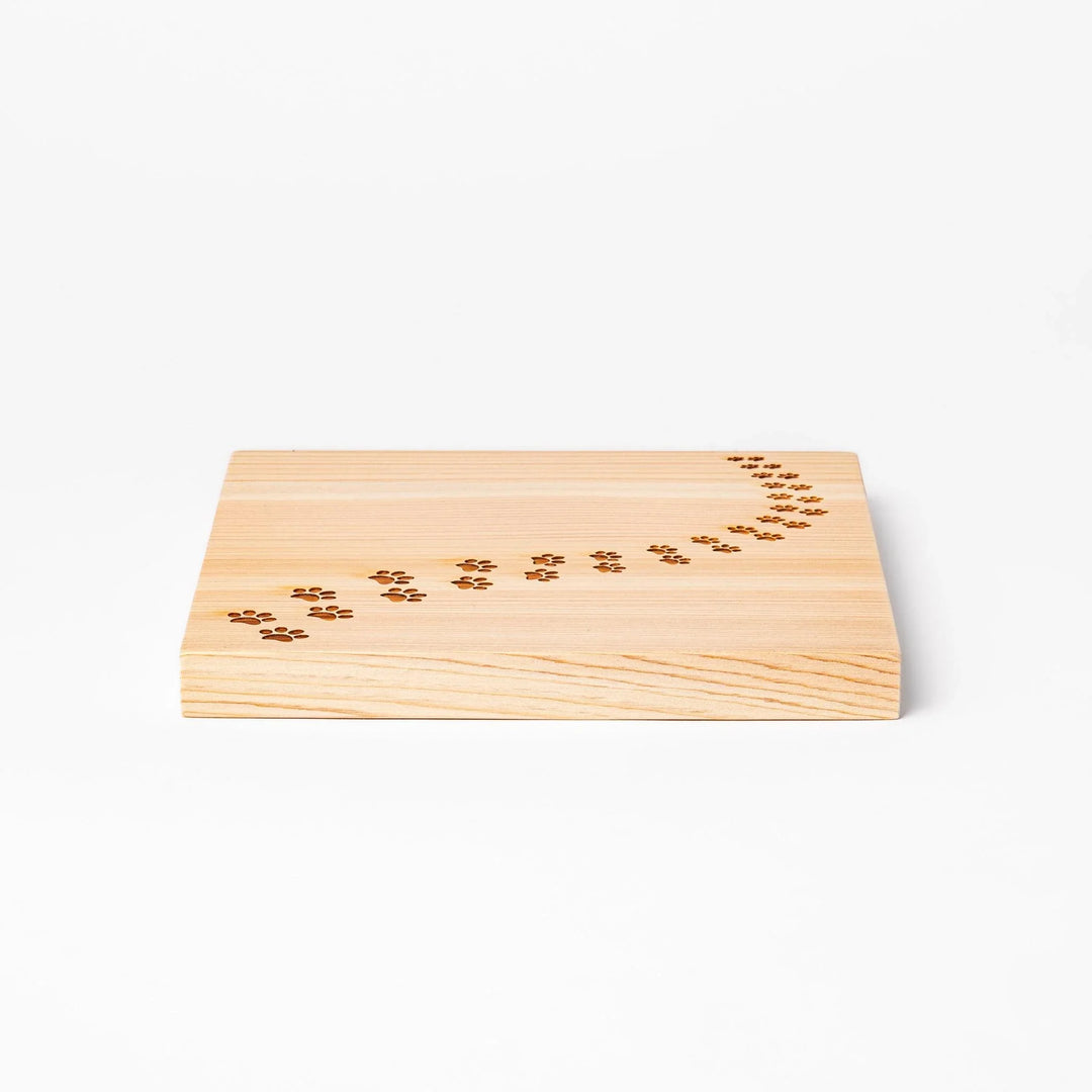 Square hinoki wood trivet featuring curved trail of laser-cut cat paw prints, protecting surfaces with charming feline design