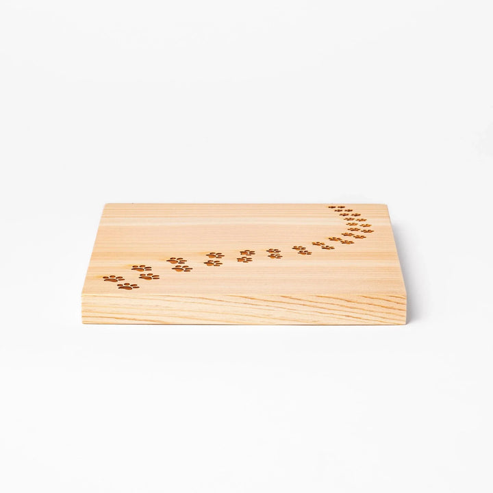 Square hinoki wood trivet featuring curved trail of laser-cut cat paw prints, protecting surfaces with charming feline design