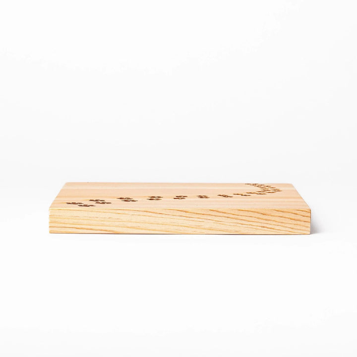 Square hinoki wood trivet featuring curved trail of laser-cut cat paw prints, protecting surfaces with charming feline design