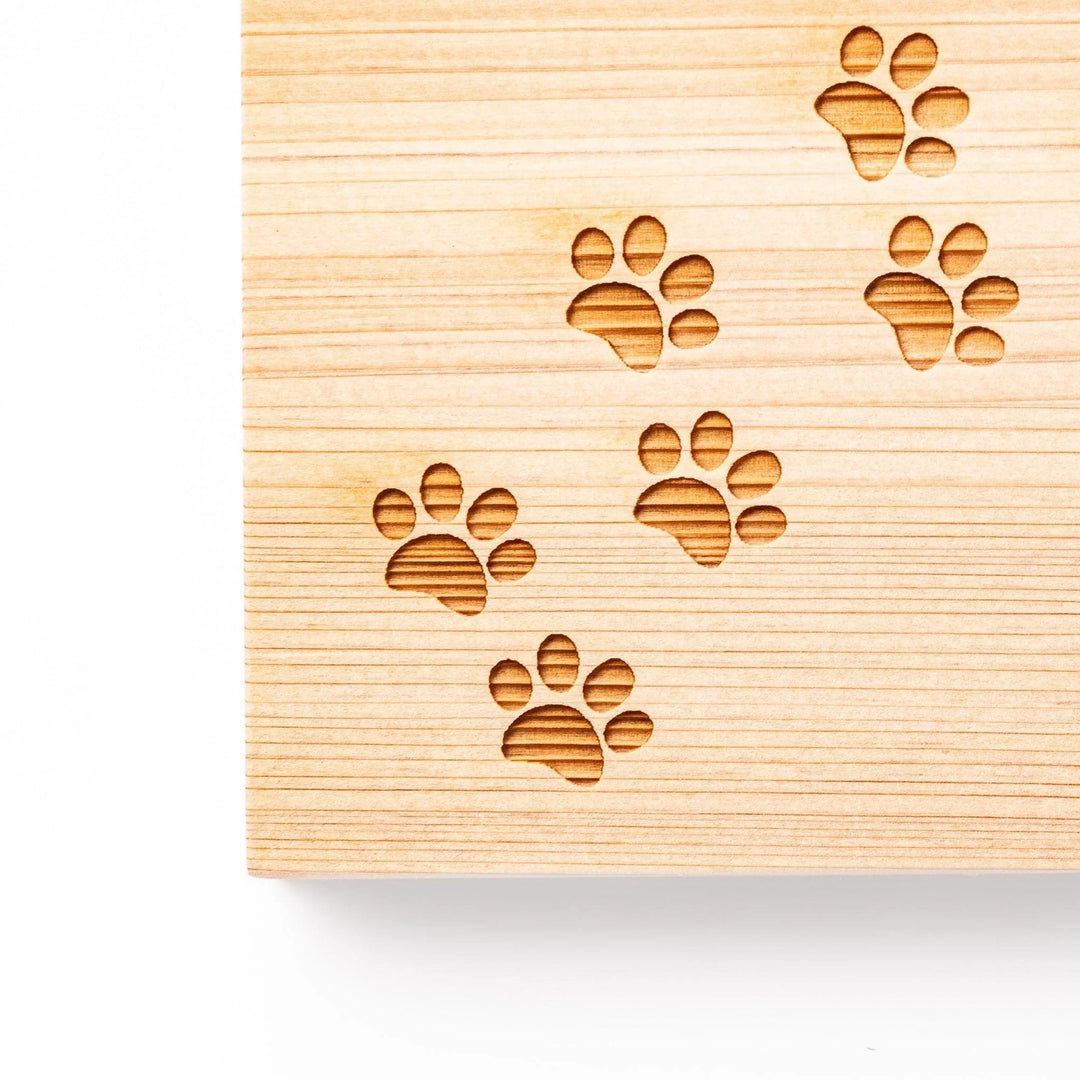 Square hinoki wood trivet featuring curved trail of laser-cut cat paw prints, protecting surfaces with charming feline design