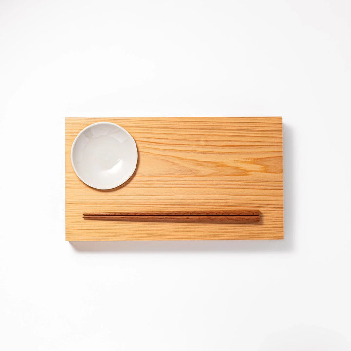 Rectangular hinoki wood sushi plate with brown cooking chopsticks and white ceramic dipping dish for elegant serving.