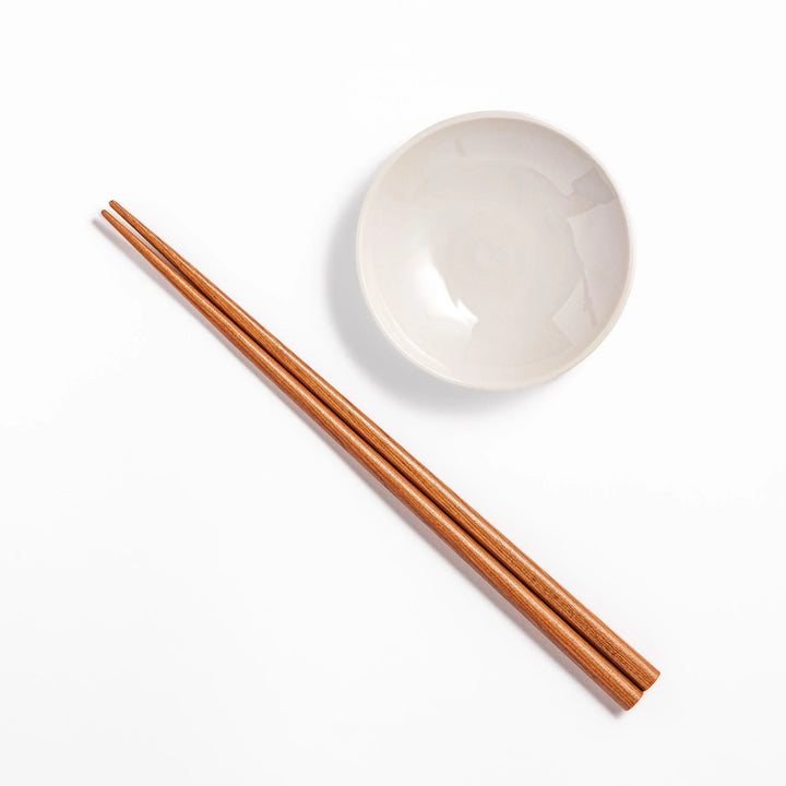 Brown chopsticks and white ceramic dipping dish on hinoki wood sushi plate for elegant sushi presentation