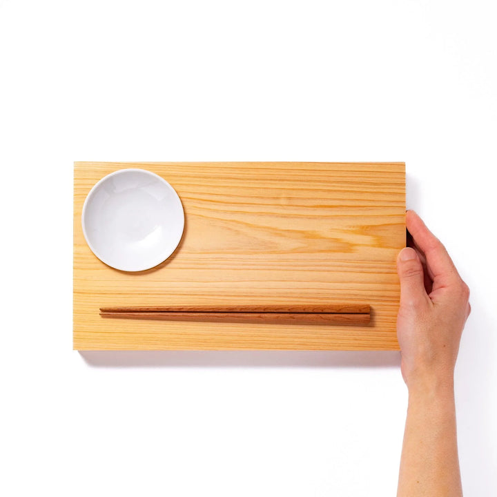 Rectangular hinoki wood sushi plate with brown cooking chopsticks and white ceramic dipping dish for elegant serving.