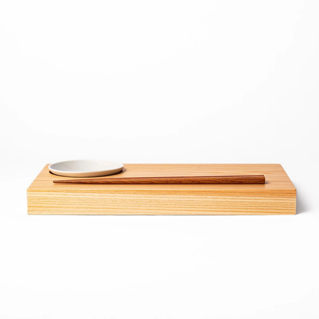 Rectangular hinoki wood sushi plate with brown cooking chopsticks and white ceramic dipping dish for elegant serving.