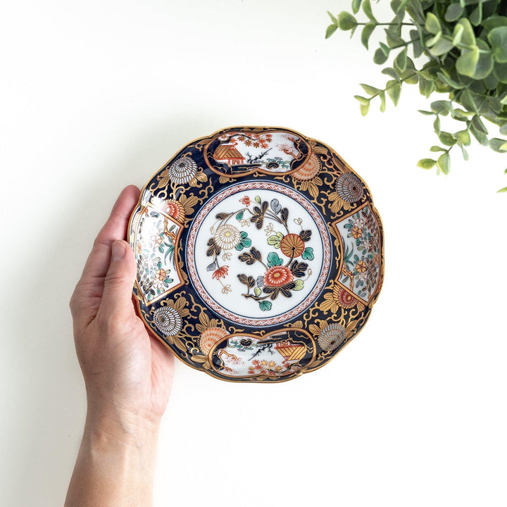 Deep round salad plate with dark blue background floral center and gold red designs of Japanese scenery.