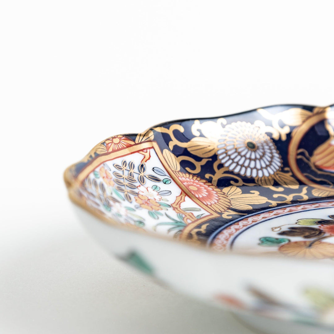 Deep round salad plate with dark blue background floral center and gold red designs of Japanese scenery.