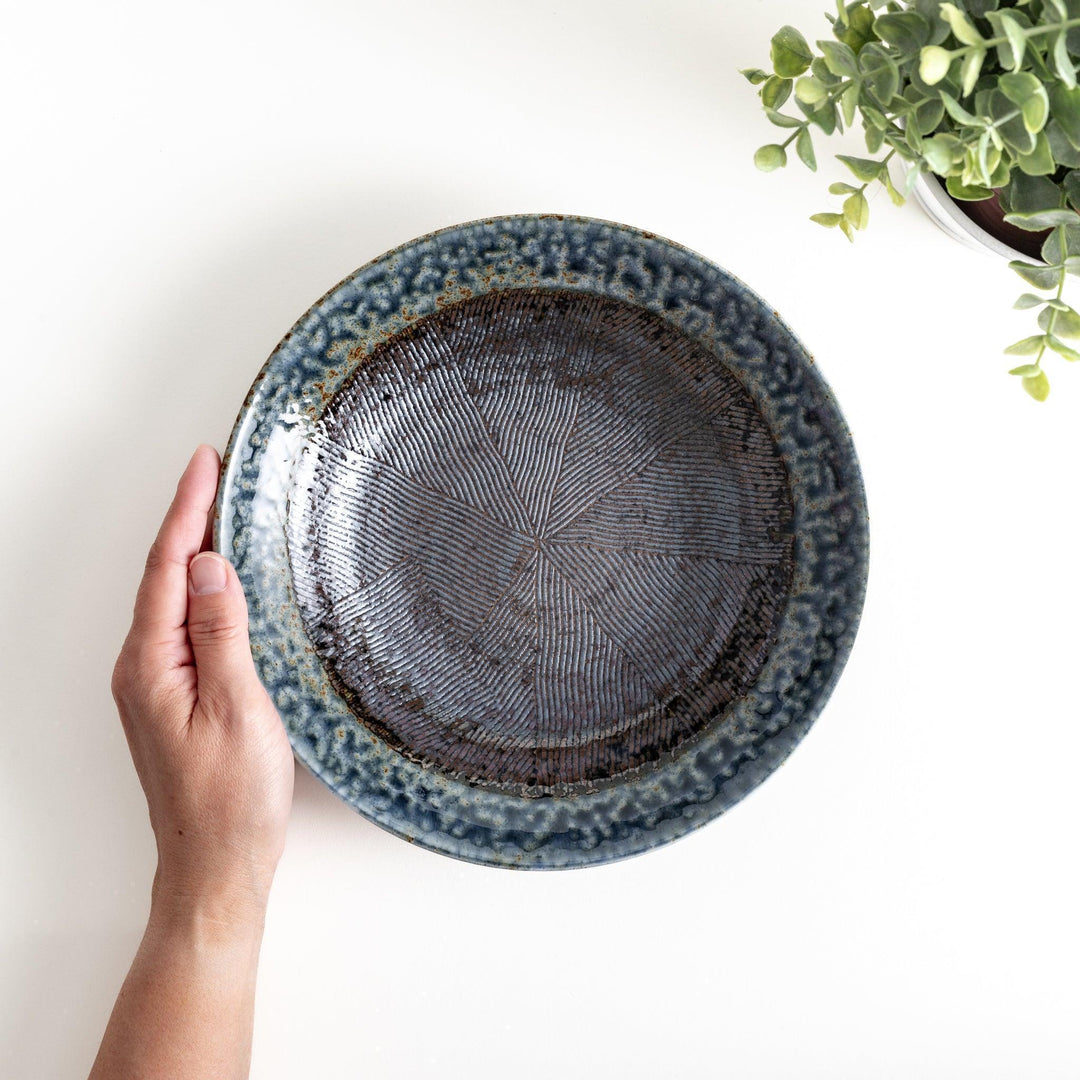 A pasta bowl with a textured glaze in blue, brown, and cream hues, featuring a ridged interior.