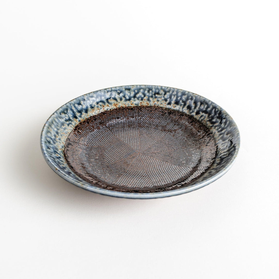 A pasta bowl with a textured glaze in blue, brown, and cream hues, featuring a ridged interior.