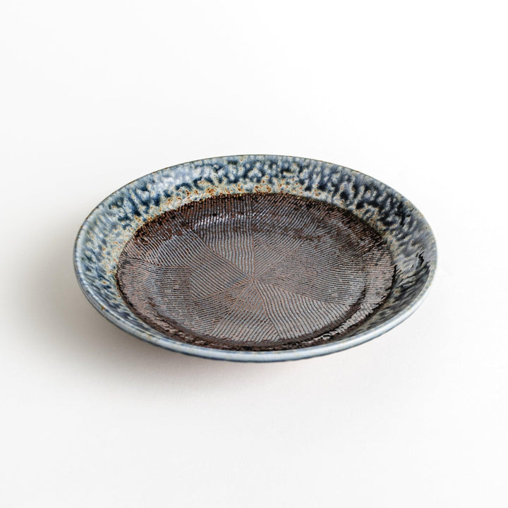 A pasta bowl with a textured glaze in blue, brown, and cream hues, featuring a ridged interior.