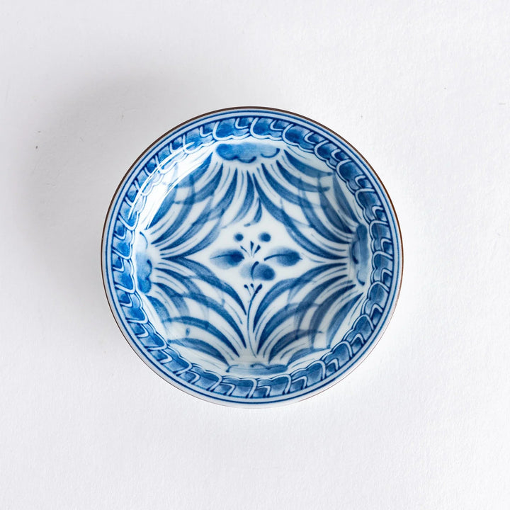 Small round Japanese dish with blue iris arabesque pattern on white background showcasing fine detailing.