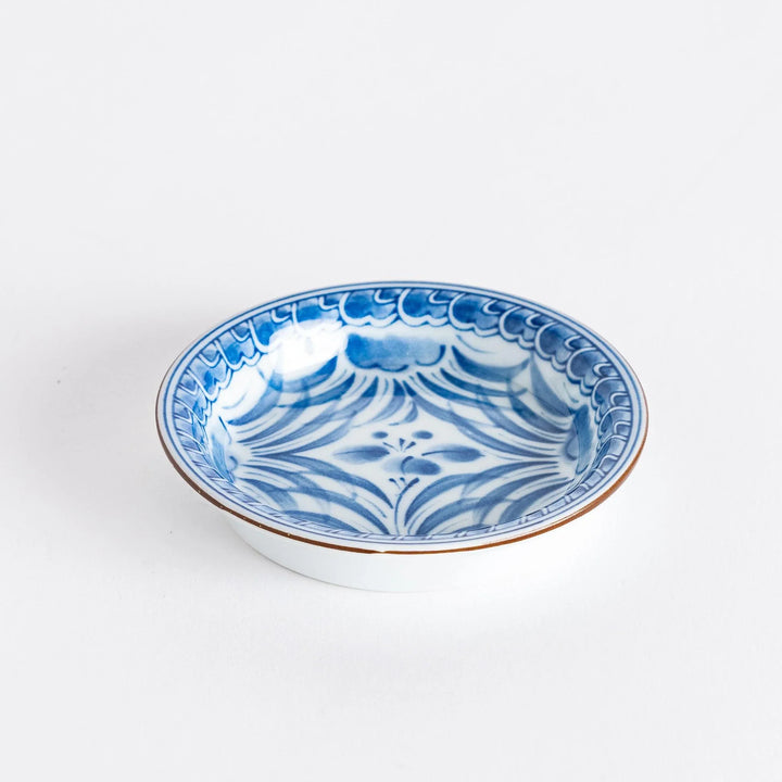 Small round Japanese dish with blue iris arabesque pattern on white background showcasing fine detailing.