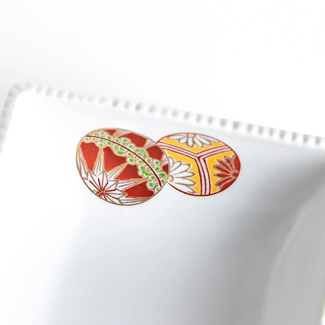 A white square bowl decorated with red and gold circular patterns.