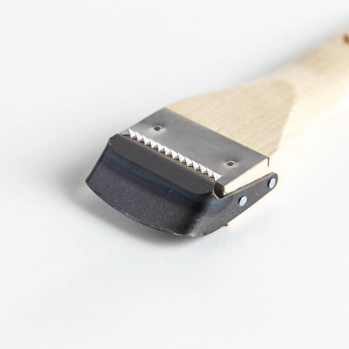 A Wood Handle Julienne Peeler, a piece of kitchenware in use to create thin vegetable strips from a carrot, perfect for salads and garnishes.