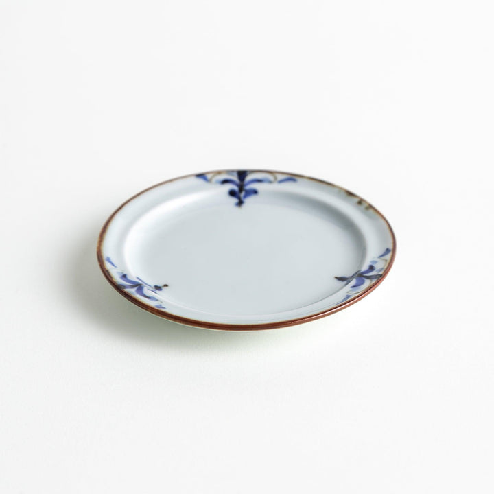 Small scalloped Japanese porcelain sauce dish with blue floral leaf pattern and brown accent trim.