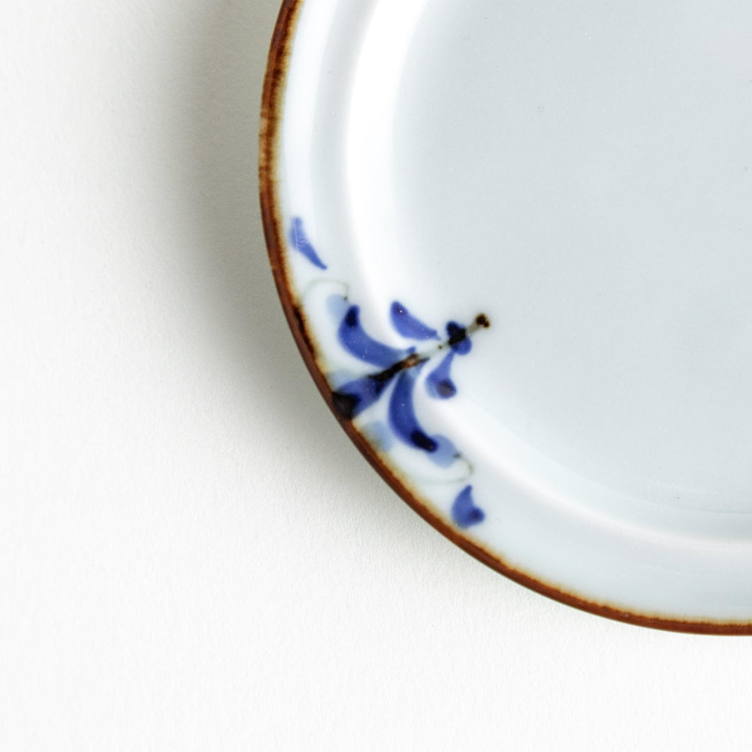 Small scalloped Japanese porcelain sauce dish with blue floral leaf pattern and brown accent trim.