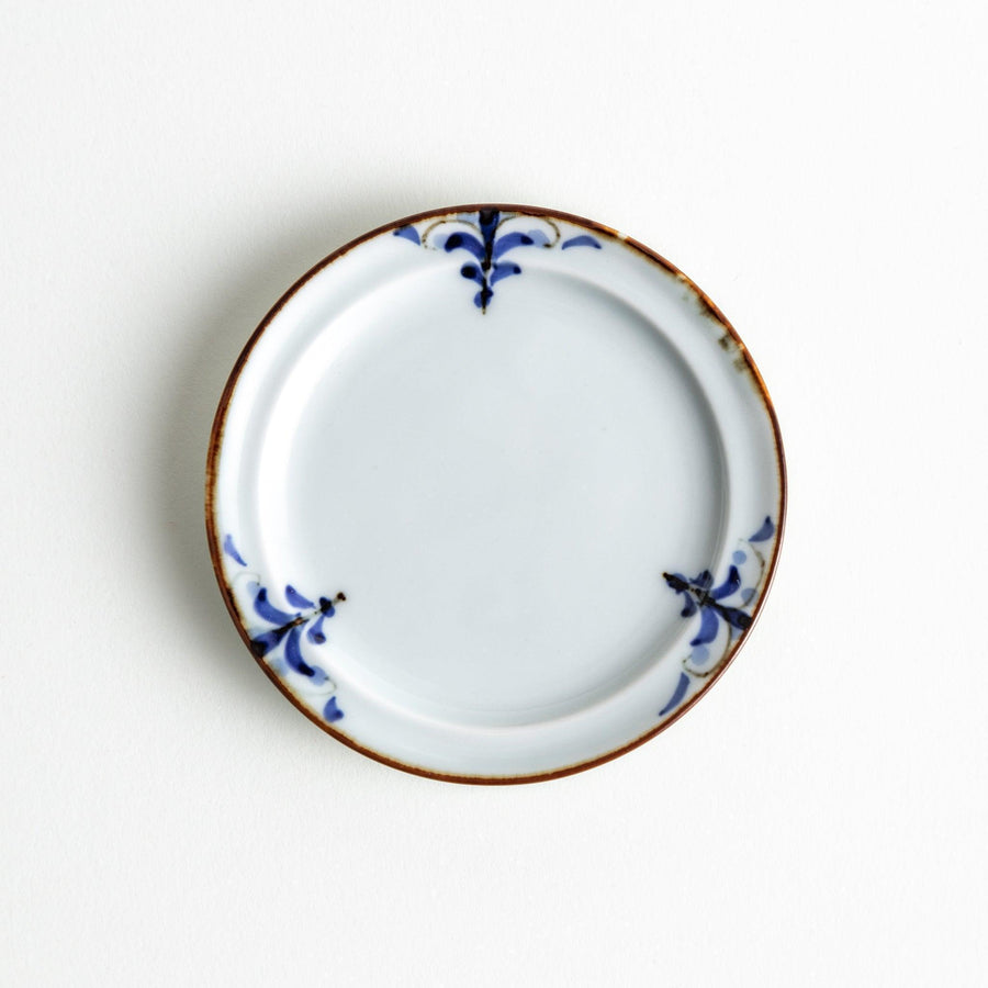 Small scalloped Japanese porcelain sauce dish with blue floral leaf pattern and brown accent trim.