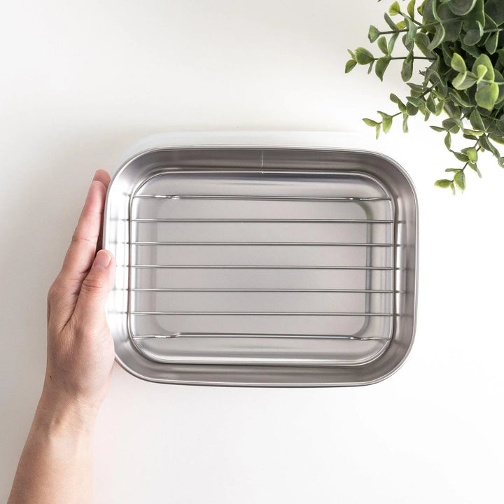 Rectangular stainless steel food prep trays with a wire rack and a white plastic lid.