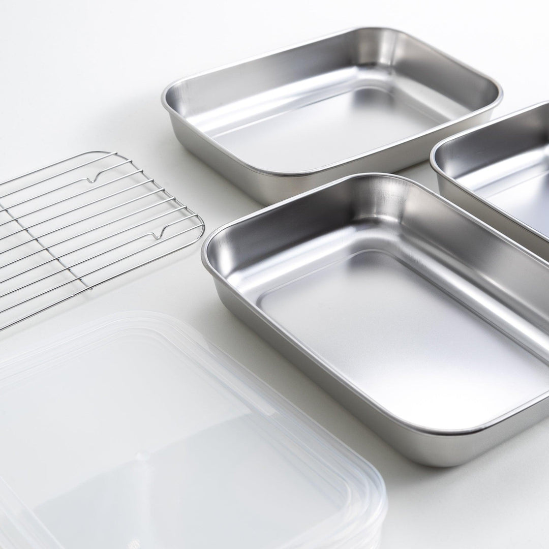 Rectangular stainless steel food prep trays with a wire rack and a white plastic lid.