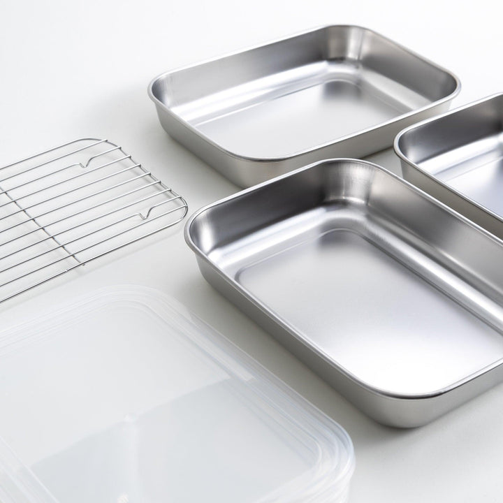 Rectangular stainless steel food prep trays with a wire rack and a white plastic lid.