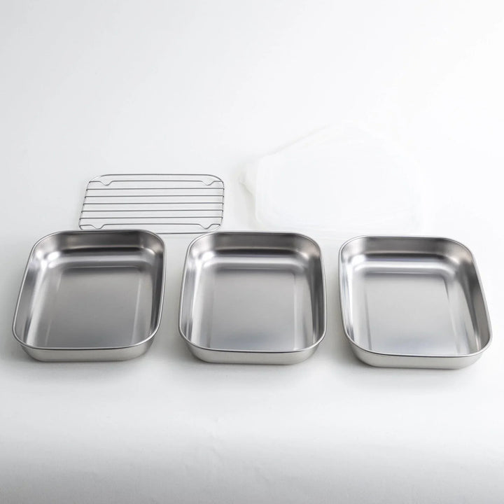Rectangular stainless steel food prep trays with a wire rack and a white plastic lid.