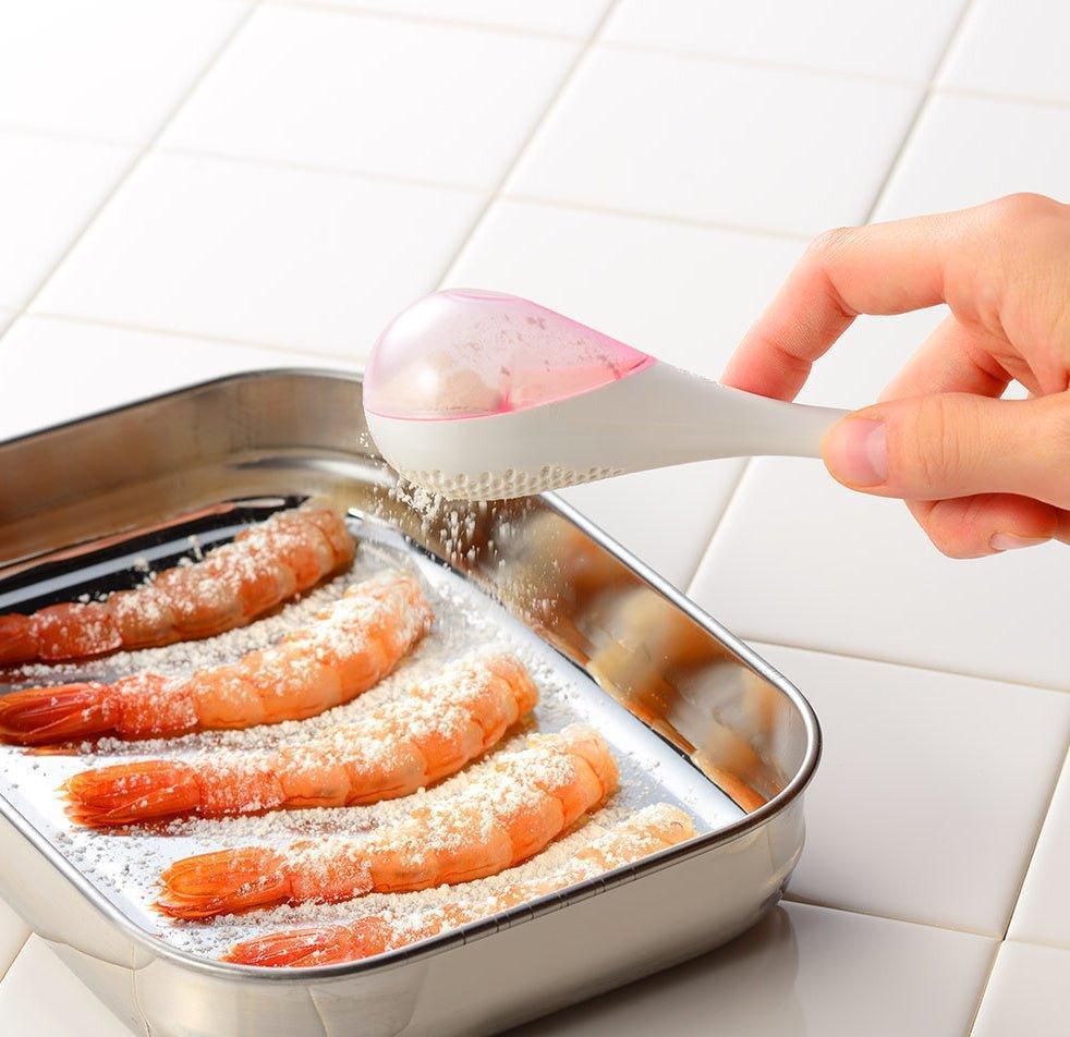 – A modern, white maraca-shaped spice sifter with a textured surface and a pink handle.