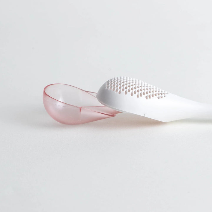 – A modern, white maraca-shaped spice sifter with a textured surface and a pink handle.