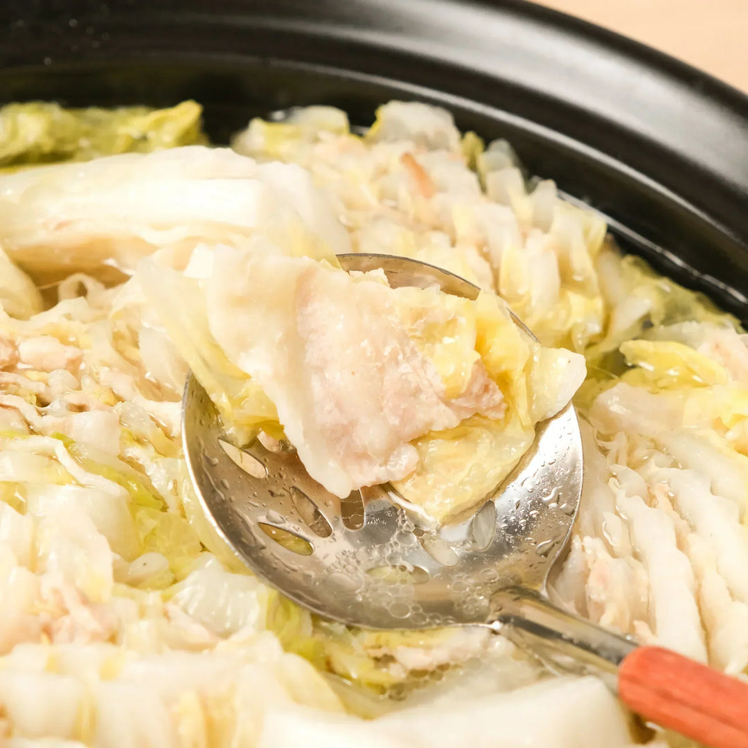 Layered napa cabbage and pork hot pot (Mille-Feuille Nabe) served in a donabe, being scooped with a slotted ladle.