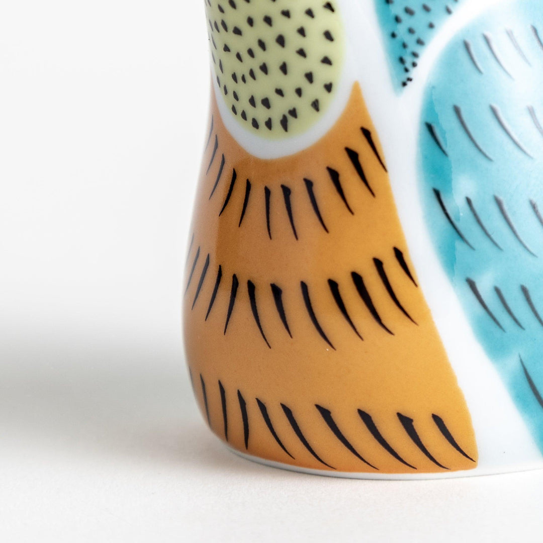 A bird-shaped ceramic soy sauce dispenser with vibrant patterns in turquoise, yellow, and green.