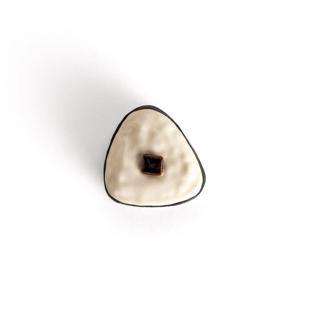 Onigiri shaped chopstick rest with white textured body black border and brown kombu detail in center.