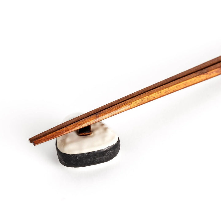 Onigiri shaped chopstick rest with white textured body black border and brown kombu detail in center.