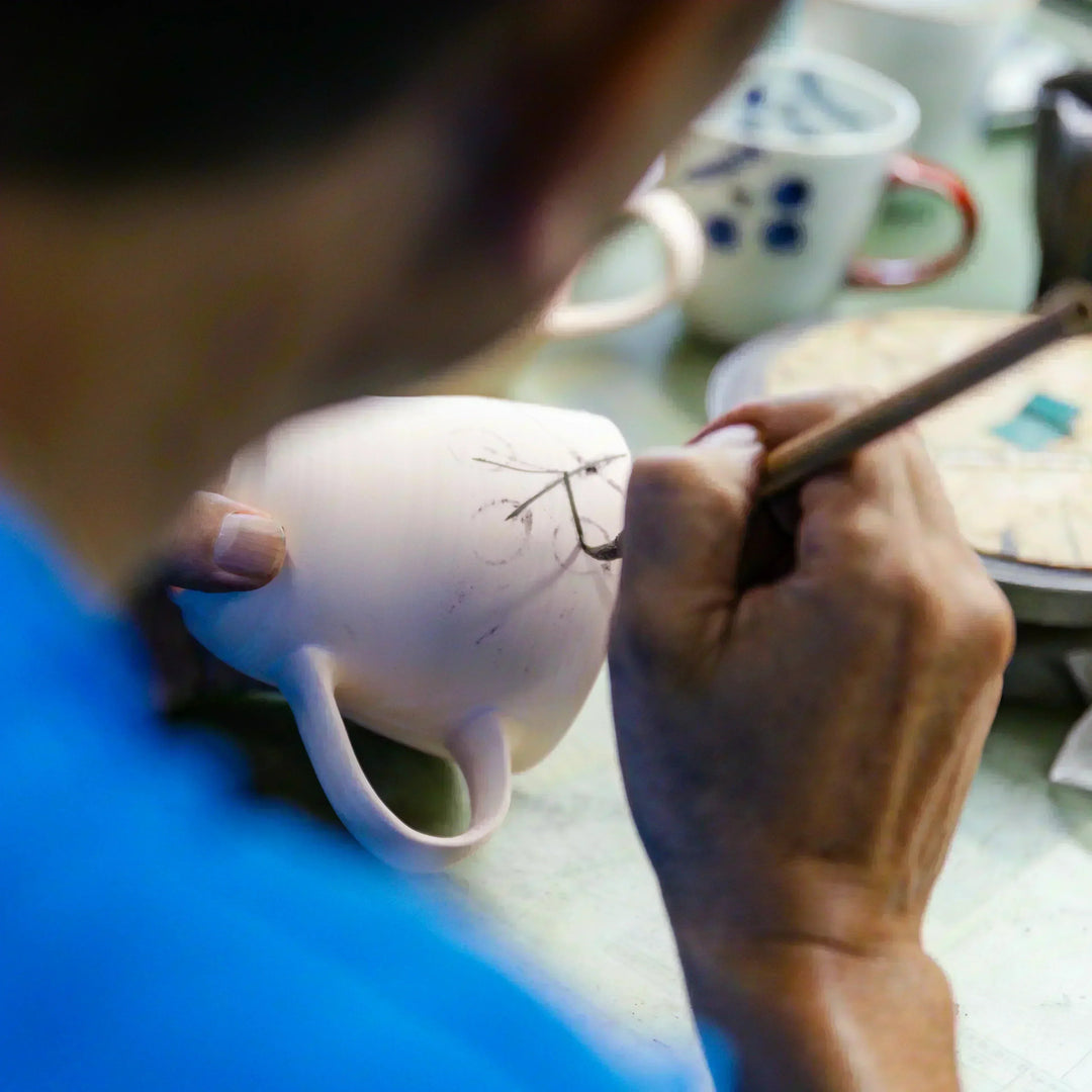 Artisan sketching a delicate design onto a ceramic mug as part of the hand painted decoration process