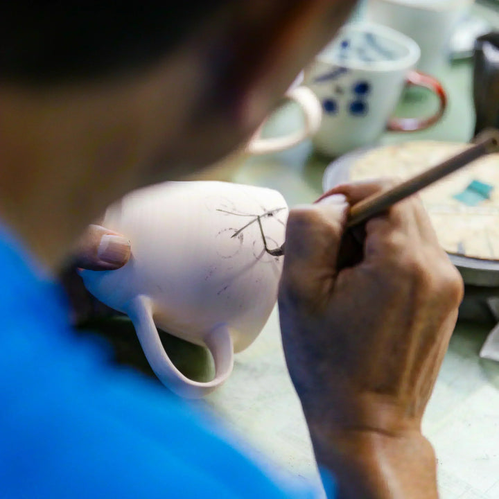 Artisan sketching a delicate design onto a ceramic mug as part of the hand painted decoration process
