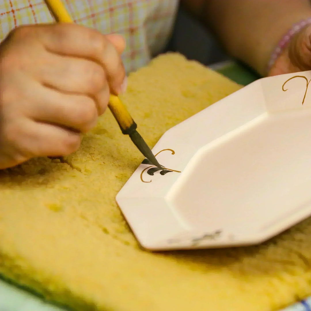 Artisan painting a decorative motif onto a ceramic plate with a brush during traditional hand decoration