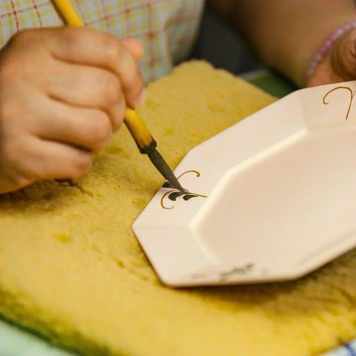 Artisan painting a decorative motif onto a ceramic plate with a brush during traditional hand decoration