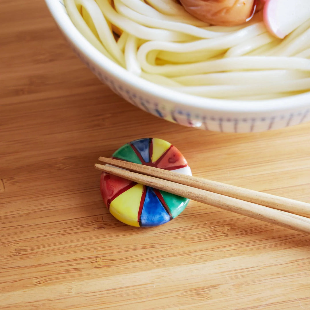 A colorful balloon-shaped chopstick rest with wooden chopsticks placed on a bamboo surface, next to a bowl of udon noodles.