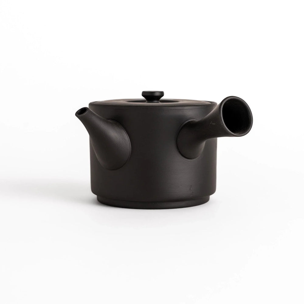 Modern black teapot with round body and horizontal spout crafted from textured ceramic for tea.