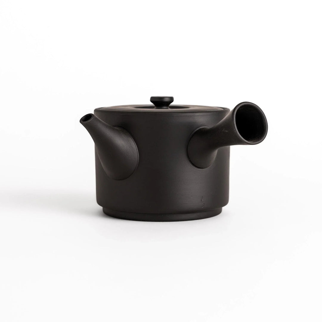 Modern black teapot with round body and horizontal spout crafted from textured ceramic for tea.