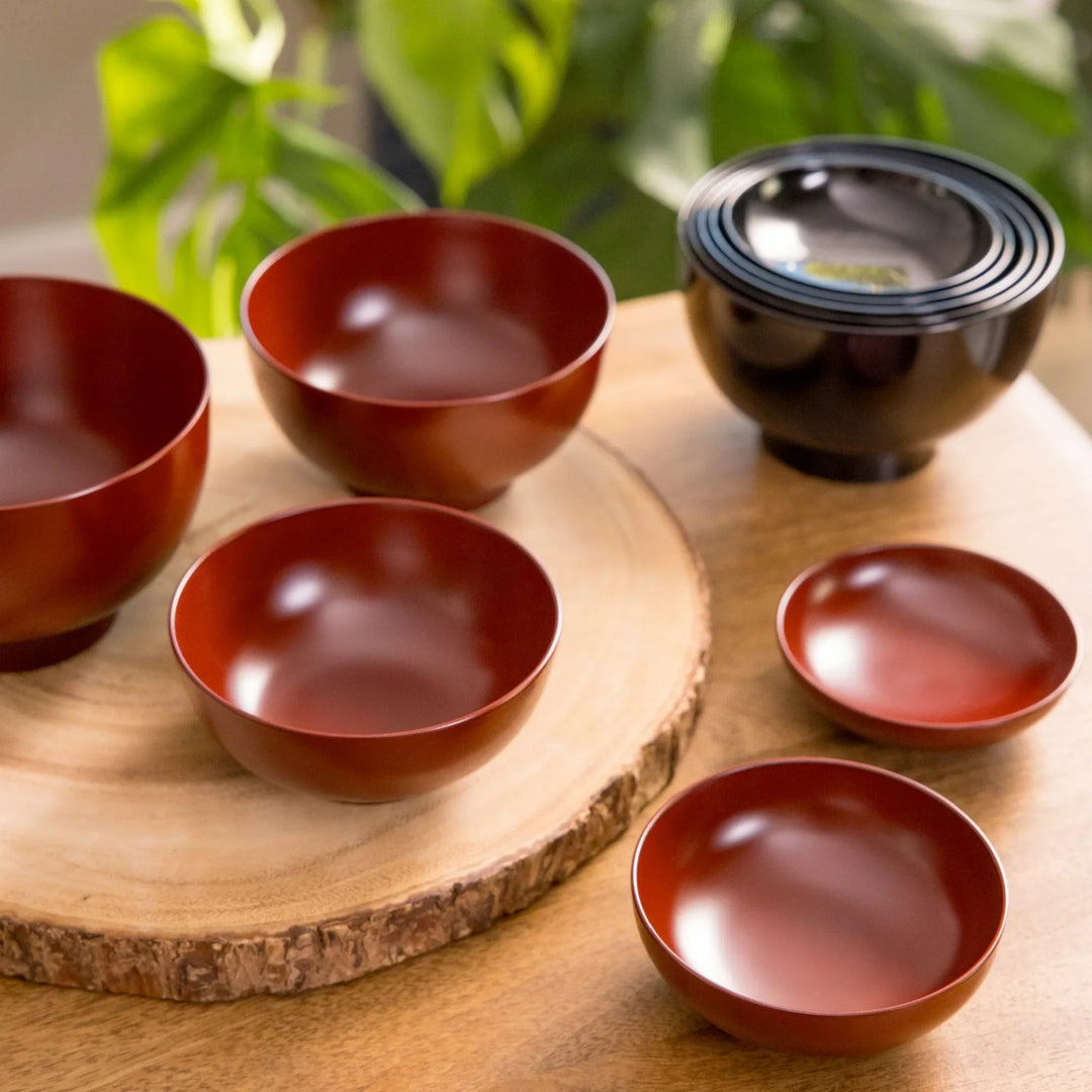Japanese five-piece nested oryoki bowl set in deep red and black lacquer, arranged on a wooden table with a warm natural tone